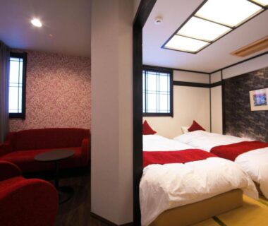Tatami room with twin low beds, red lounge seating and shoji-style windows at Yunosato Hayama in Ōita