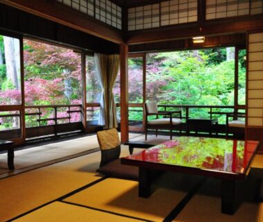 Traditional tatami room with lacquered table, zabuton cushions, shoji screens and lush garden view through open veranda