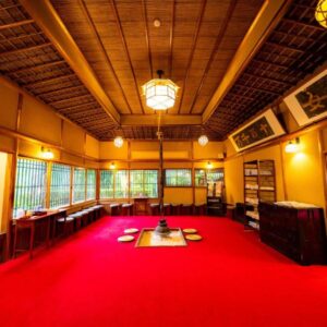 Spacious communal hall with red carpet, sunken hearth, wooden ceiling and shoji windows at Yunoshimakan, Gifu