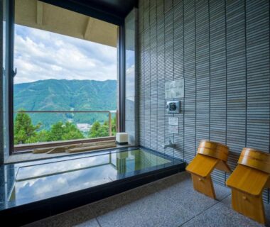 Indoor onsen bath with wooden stools and large window overlooking mountains and valley at Yunoshimakan Gifu