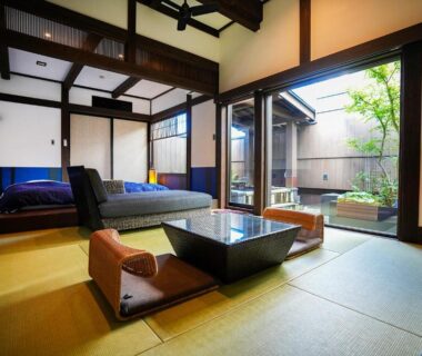 Tatami room with low table, zabuton cushions, futon bed and sliding shoji doors opening to a small courtyard garden