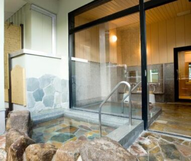 Indoor stone onsen bath with glass partition and wooden ceiling at Yura No Yado Seifuen in Nagano