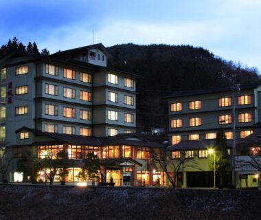 Lit multi-story ryokan exterior of Yura No Yado Seifuen with mountain backdrop in Nagano