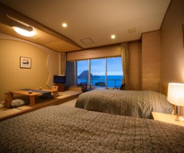 Twin beds with tatami seating and low table, water view at Yura Onsen Yaotome, Yamagata.
