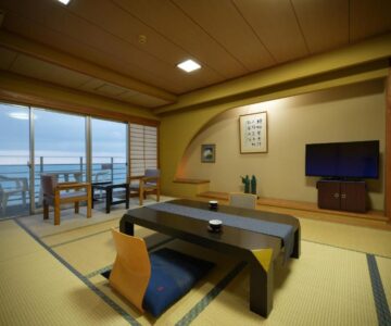 Spacious tatami room with low table and balcony overlooking coastal waters at Yura Onsen Yaotome Yamagata