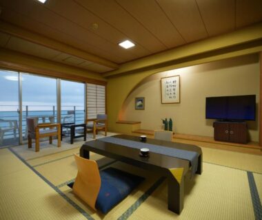 Spacious tatami room with low table and balcony overlooking coastal waters at Yura Onsen Yaotome Yamagata