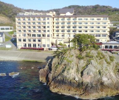 Multi-story ryokan perched on rocky coastline with ocean and hillside in Yamagata Tōhoku Japan
