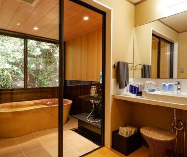 Japanese-style bathroom with wooden soaking tub, washbasin, and garden view at Yuraku Kinosaki Spa in Hyōgo