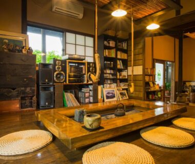 Tatami seating area with low wooden table, round straw cushions and bookshelf at Yurari Rokumyo in Ōita, Kyūshū