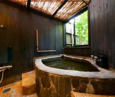 Indoor stone soaking tub with wooden walls and shower at Yurari Rokumyo, Oita, Kyushu, Japan