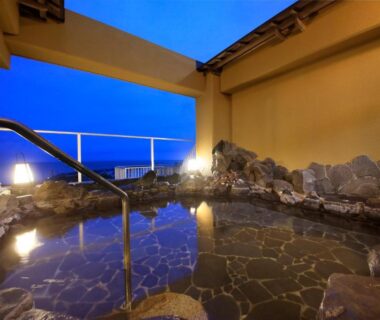 Stone-lined onsen bath with handrail under open roof at Yururi Nishiizu, Shizuoka, Chūbu