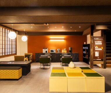 Communal lounge with shoji screens, low seating, pendant lights and reception area at Yusai Bekkan, Kumamoto