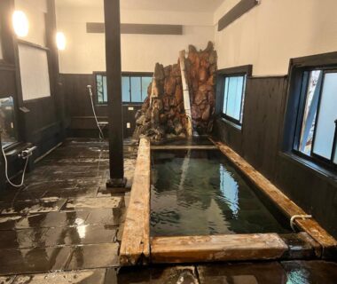 Indoor wooden onsen bath with stone floor and windows at Yusai Bekkan Kumamoto
