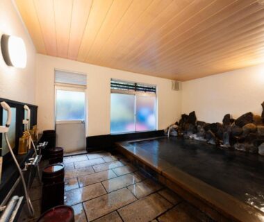 Stone-lined indoor onsen with wooden ceiling and washing stations at Yusai Bekkan in Kumamoto, Kyūshū, Japan