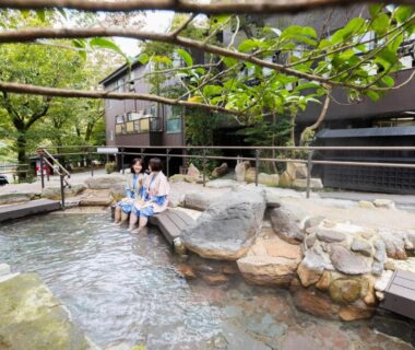 Guests in yukata enjoying a stone communal footbath at Yusai Bekkan surrounded by trees and traditional buildings in Kumamoto