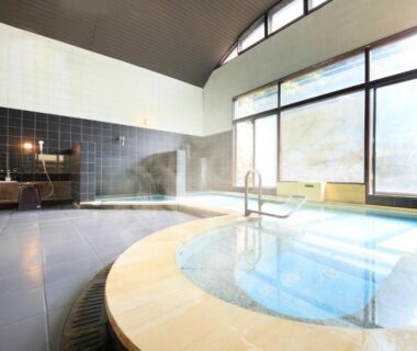 Large indoor tiled soaking pool with shower stations at Yutorelo Beppu in Oita, Kyushu