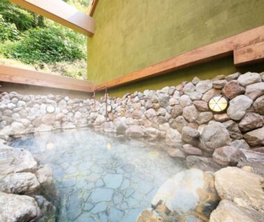 Stone-lined outdoor onsen bath with steaming clear water and wooden ledge, Yutorelo Beppu Oita