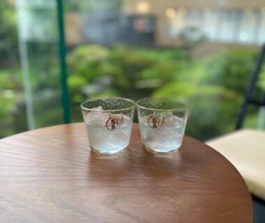 Two glass tumblers on round wooden table overlooking a blurred garden view at Yutorelo Beppu, Ōita
