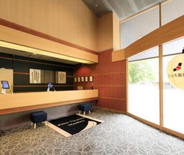 Ryokan reception with wooden counter, low stools, paper lantern, floor-to-ceiling window and stone-patterned flooring