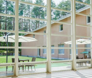 Floor-to-ceiling windows overlooking courtyard with umbrellas and lawn at Yutorelo Tateshina Hotel Nagano