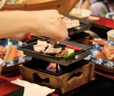 Hand grilling meat slices on tabletop brazier amid assorted Japanese dining dishes at Yutorelo Toyako, Hokkaidō