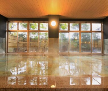 Spacious indoor onsen with wooden ceiling, large windows and garden view at Yutorelo Yamaga in Kumamoto