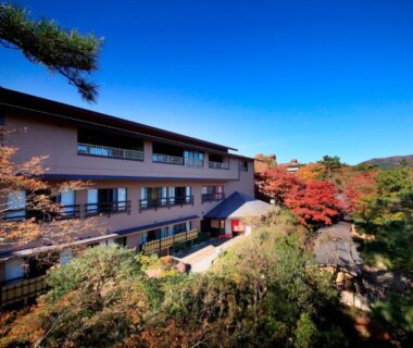 Exterior of Yutorelo-an ryokan framed by autumn foliage and balconies under a clear blue sky in Kanagawa, Kantō