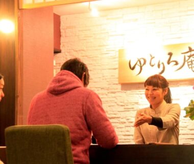Reception staff greeting guests at Yutorelo-an with illuminated Japanese sign and seating area