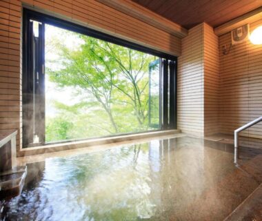 Indoor onsen with steaming tiled bath and large window overlooking green trees at Yutorelo-an ANNEX