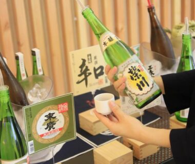 Hand holding cup beside sake bottles on display at Yutoriro Bandai Atami Fukushima