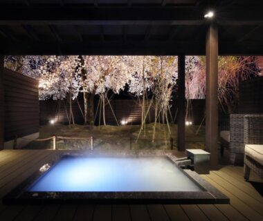 Outdoor onsen bath on wooden deck framed by illuminated cherry trees at Yuuyu No Sato Yusa, Yamagata