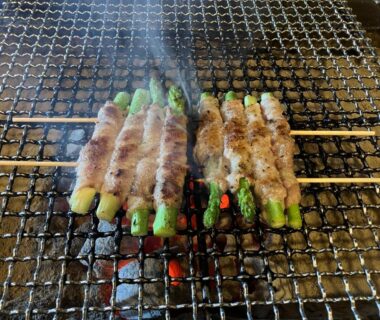 Skewers of asparagus wrapped in meat grilling over charcoal at Yuuzuru ryokan in Shizuoka Chūbu