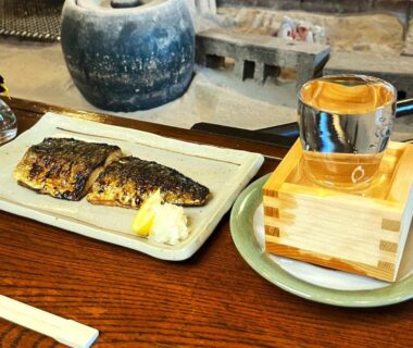 Grilled fish with lemon and overflowing sake glass in a masu on wooden table at Yuuzuru, Shizuoka