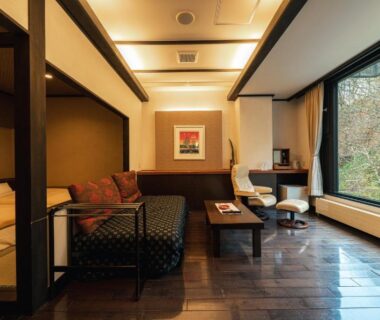 Wooden floored guest room with sofa, low table, bed platform and large window overlooking greenery at Yuyado DAIICHI Hokkaidō