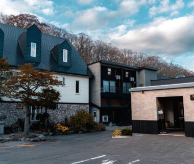 Facade of Yuyado DAIICHI with driveway, entrance sign, autumn trees and wooded hills in Hokkaidō