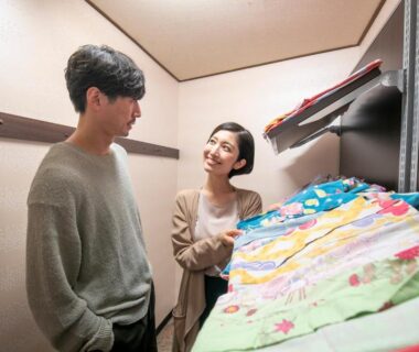 Guests inspecting colorful stacked futon bedding in a compact ryokan room at Yuyado Ichibanchi, Shizuoka