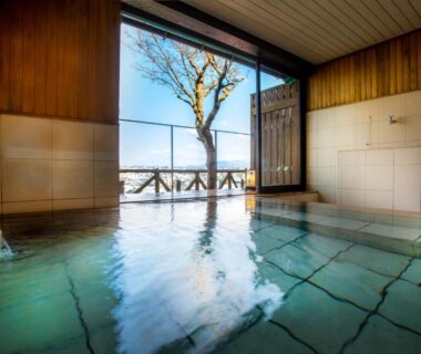 Indoor tiled onsen bath with wooden walls and large window overlooking a tree and distant landscape, Yuyaruru Saisai, Ishikawa Japan