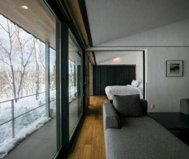 Sofa, wooden floor and low bed with floor-to-ceiling glass windows overlooking snow at Zaborin Hokkaido