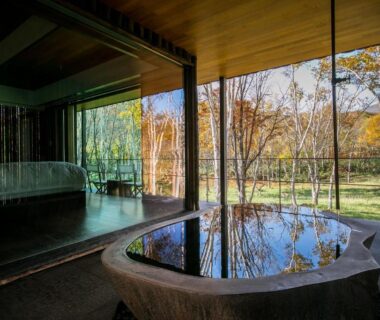 Stone soaking tub by floor-to-ceiling window beside a bed, garden and trees visible outside at Zaborin Hokkaidō