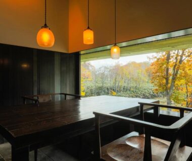 Wooden dining table with pendant lights and large window framing autumn foliage at Zaborin in Hokkaidō