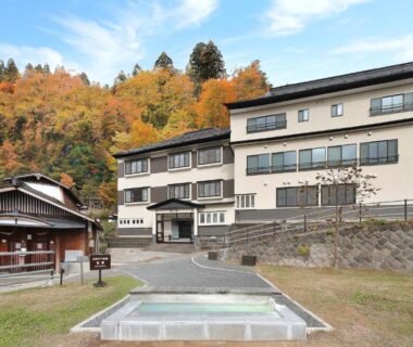 Multi-story ryokan building with outdoor footbath and autumn trees in Yamagata's Zao Onsen area