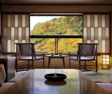 Tatami room with low table and chairs overlooking autumn foliage at Zao Onsen Omiya Ryokan, Yamagata
