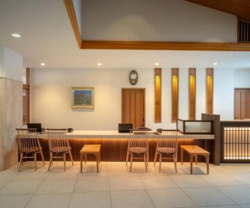 Warm wooden reception desk with stools, ambient lighting and tiled floor at Zao Shiki no Hotel lobby in Yamagata