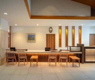 Warm wooden reception desk with stools, ambient lighting and tiled floor at Zao Shiki no Hotel lobby in Yamagata