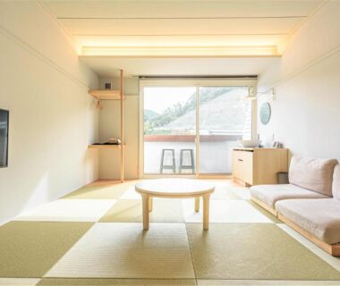 Bright tatami room with low table, sofa, wall TV and balcony overlooking hills at Zen no Yu Shizuoka