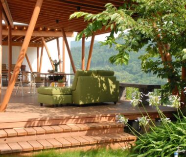 Outdoor wooden terrace with green seating, wooden beams and garden foliage at Zen no Yu in Shizuoka