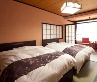 Twin beds on tatami flooring with shoji screens and seating area at caffel Hina-no-sato in Ōita