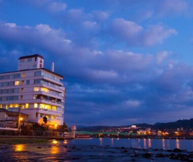 Dusk waterfront ryokan with illuminated windows and water reflections, caffel Hina-no-sato, Ōita Kyūshū Japan