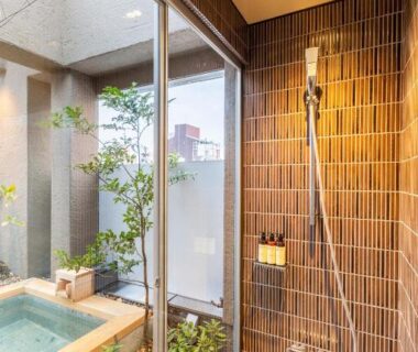 Shower beside wooden soaking tub with glass courtyard and plants at cyashitsu ryokan asakusa Tokyo
