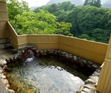 Stone-lined outdoor onsen bath with bamboo fence and forest view at kinugawaonsen Fukumatsu, Tochigi